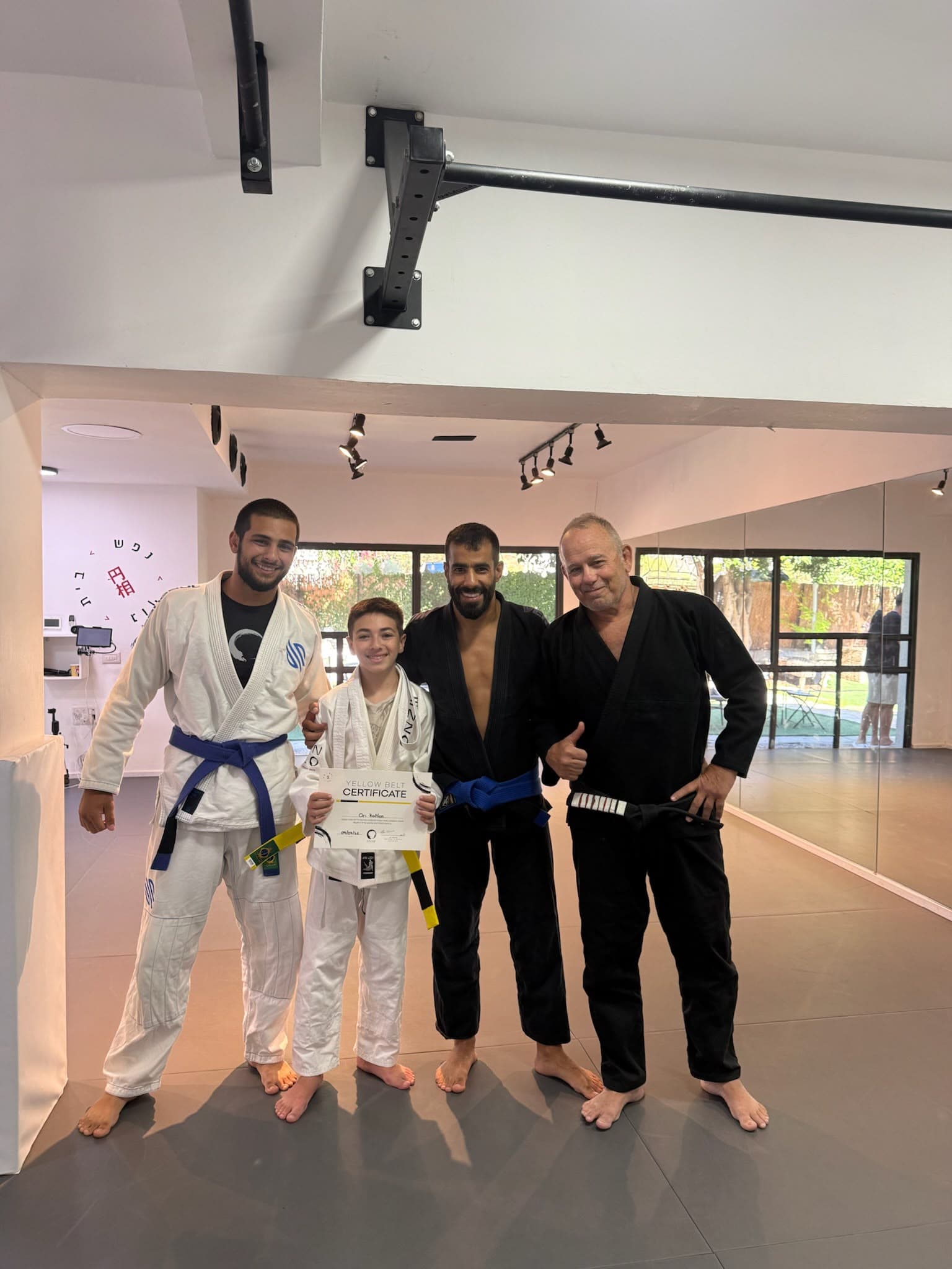 שלושה מאמנים עם ילדה בחליפת ג׳יו ג׳יטסו בסטודיו