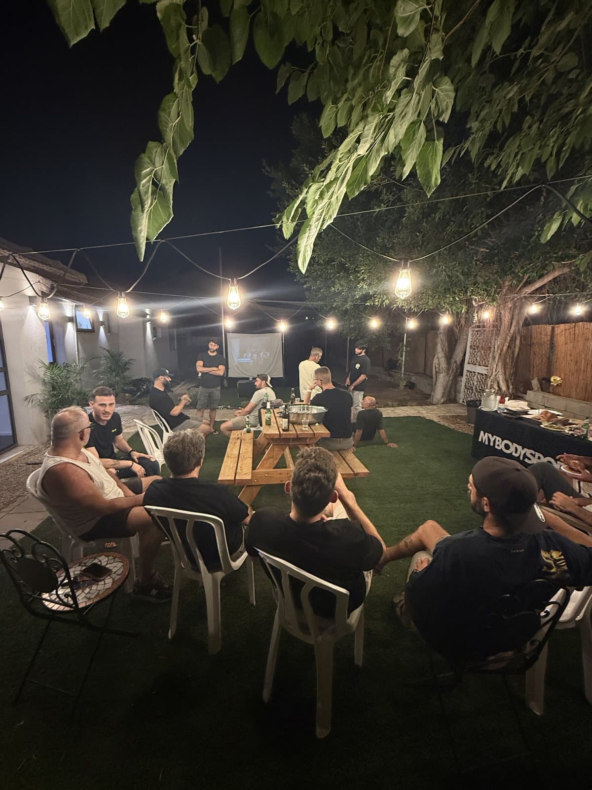 ערב קהילה בחצר: אנשים יושבים במעגל תחת שרשרת נורות